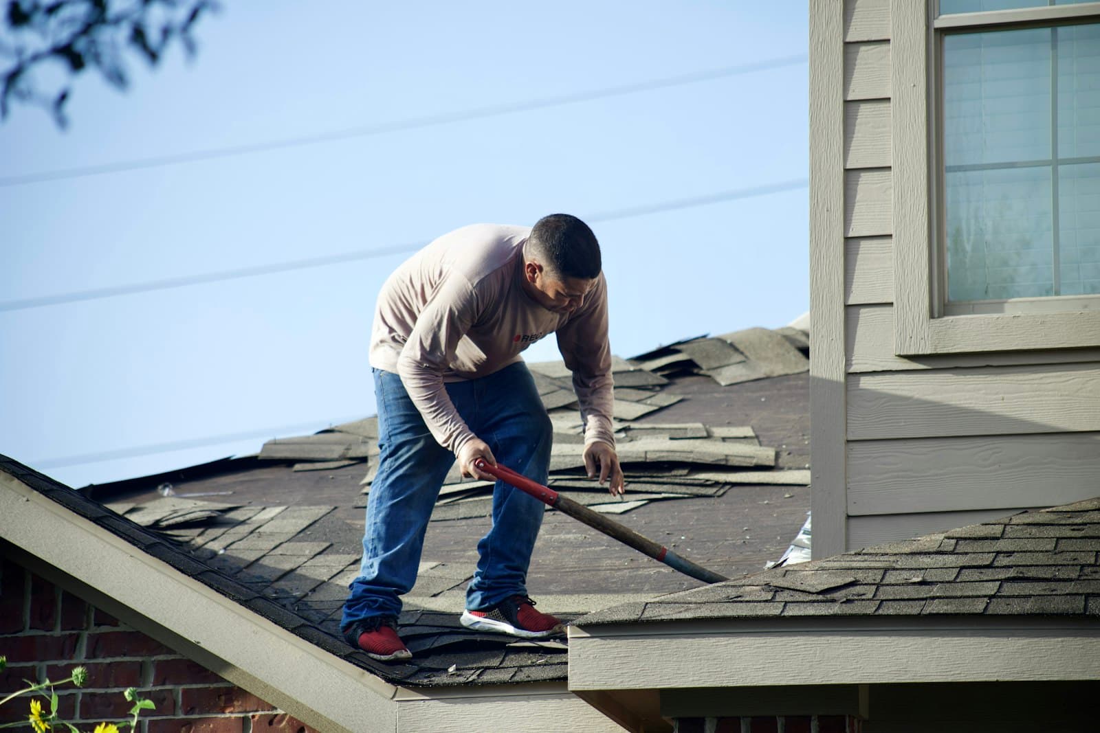Roofer tearing old composition shingles off a home during a roof replacement